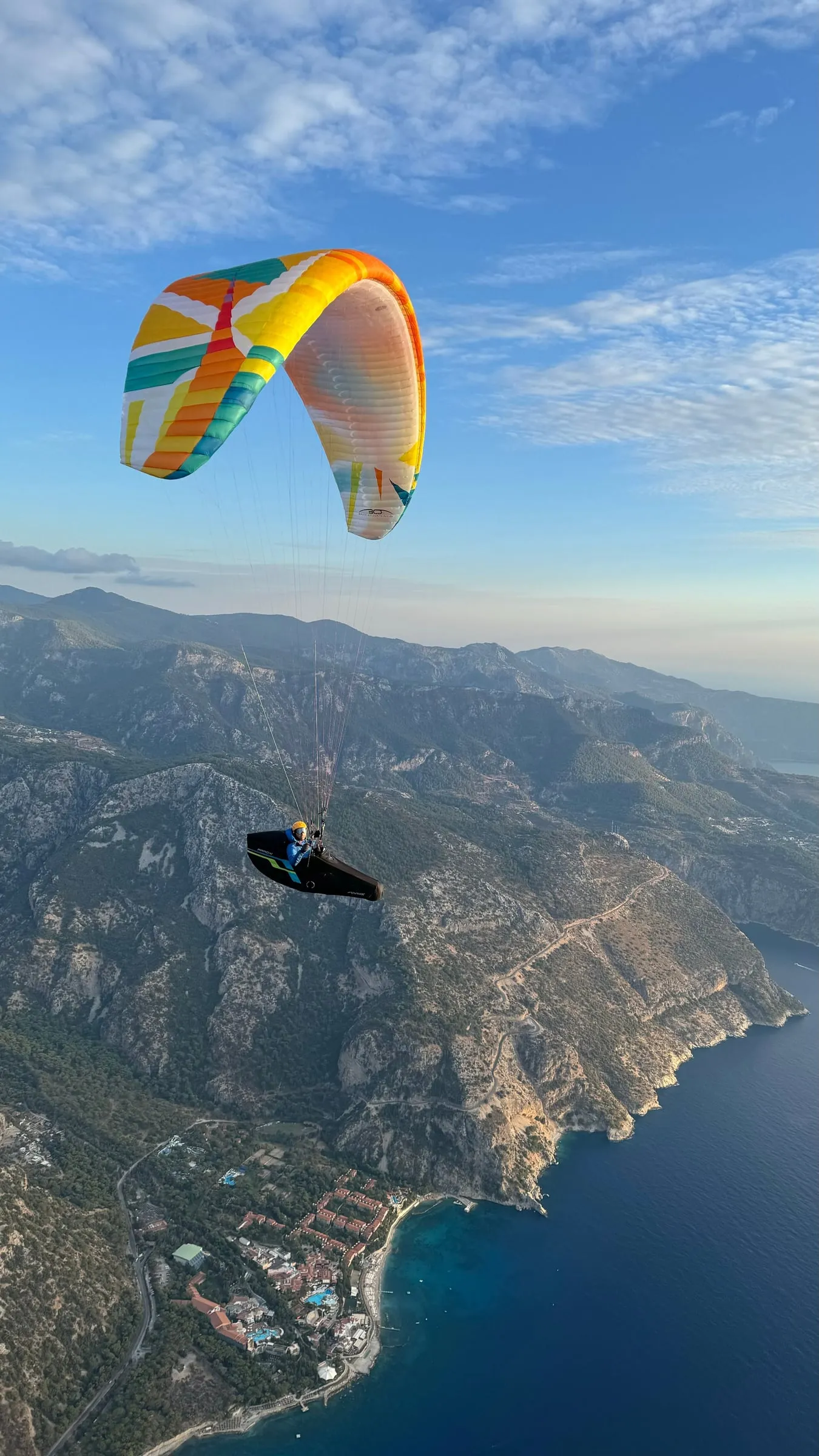 Shahin flying a colourful paraglider high above a mountainous coastline